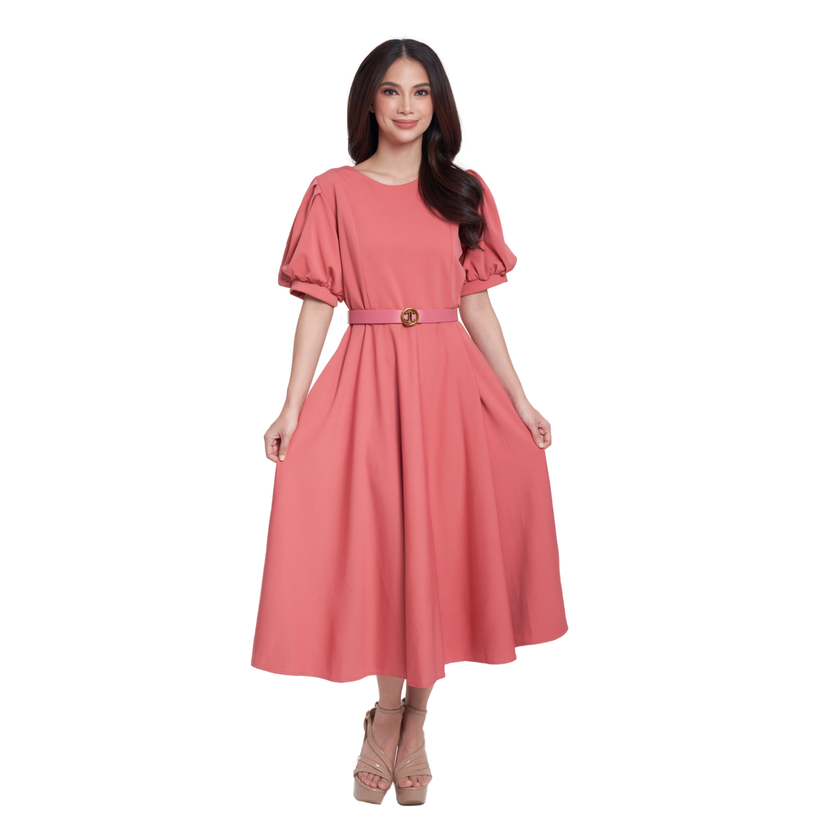 A woman modeling a dusty pink midi dress with puff sleeves, a matching waist belt with a gold buckle, and beige high-heeled sandals, set against a plain white background.
