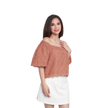 A woman modeling a terracotta-colored off-the-shoulder eyelet lace top with short flutter sleeves, paired with a white skirt, against a plain white background.
