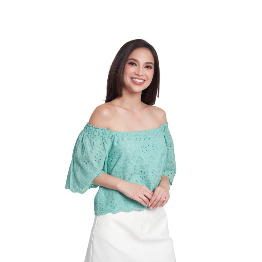 A woman modeling an off-the-shoulder mint green eyelet lace top with puff sleeves, paired with a white skirt, against a plain white background.