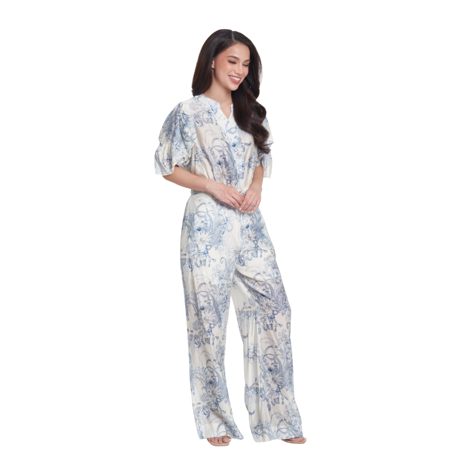 A woman modeling a light blue and white floral print jumpsuit with short puff sleeves and wide legs, set against a plain white background.