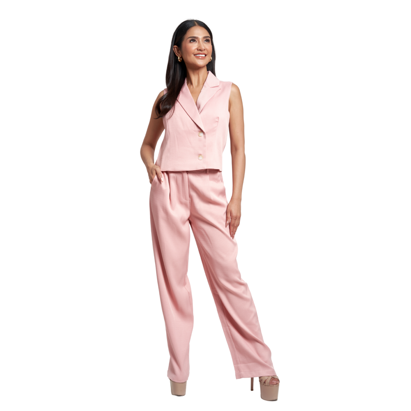A woman modeling a light pink two-piece suit consisting of a sleeveless double-breasted blazer and matching wide-leg trousers, set against a plain white background.