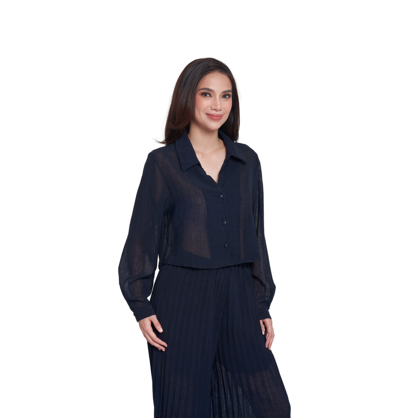 A woman modeling a dark navy blue sheer long-sleeve button-up shirt paired with matching pleated trousers, set against a plain white background.